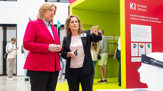 Susan Beudt, stellvertretende Leiterin des Educational Technology Lab am DFKI und Konsortialleiterin des Projekts KI-Kompass Inklusiv (r.), erläutert Bundesministerin Bärbel Bas (l.), wie KI-gestützte Assistenztechnologien Menschen mit Behinderungen im Arbeitsleben unterstützen können.