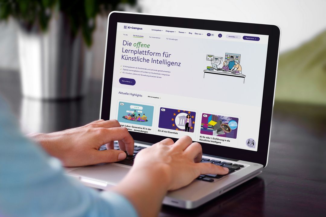 Das Bild zeigt eine Person, die an einem Laptop arbeitet. Man erkennt nicht, welches Geschlecht diese Person hat. Auf dem Laptop sieht man die KI-Campus Lernplattform. Auf der Plattform steht: Die offene Lernplattform für Künstliche Intelligenz. Man sieht außerdem ein paar der Kursangebote der Plattform,einer davon heißt 