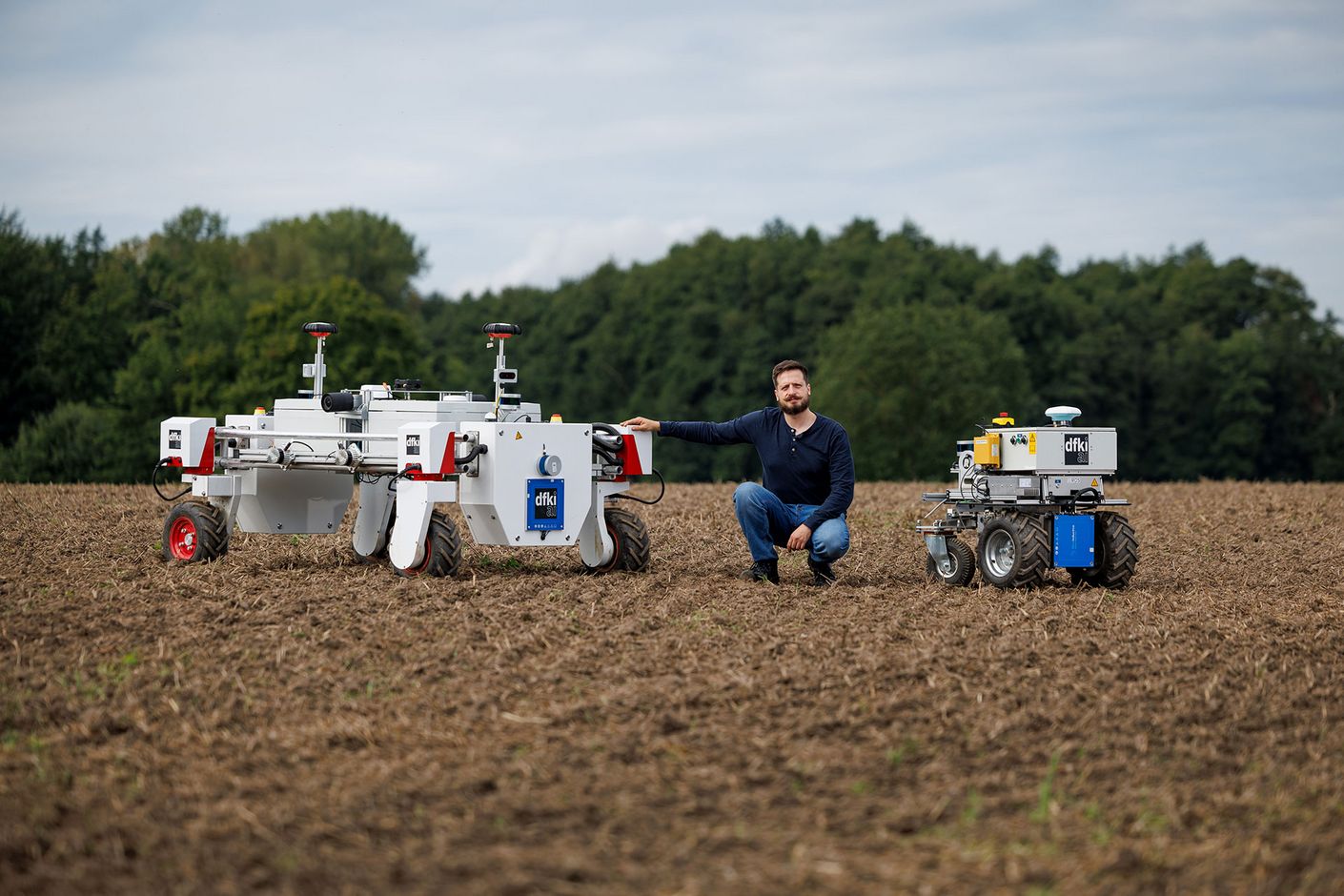 Wissenschaftler Kisliuk zwischen zwei Robotern auf dem Feld