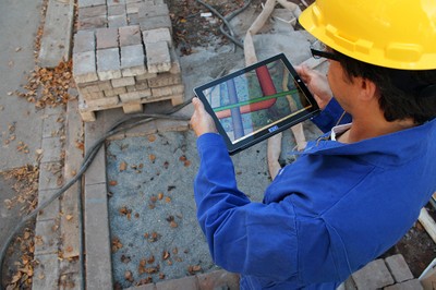 Bauarbeiter mit iPad, im Hintergrund eine Baustelle.